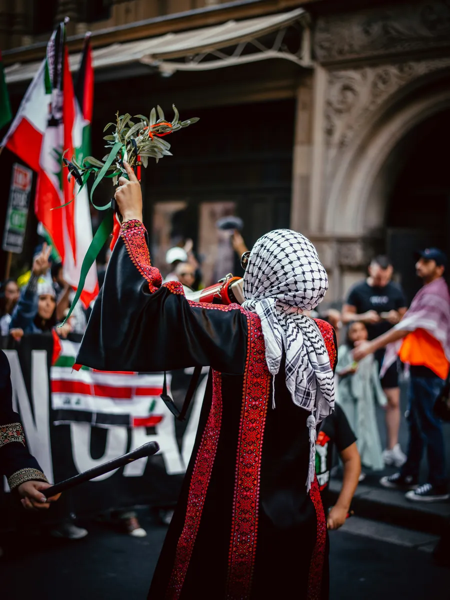 Demonstrator in traditional Palestinian embroidery raising flowers at a street protest